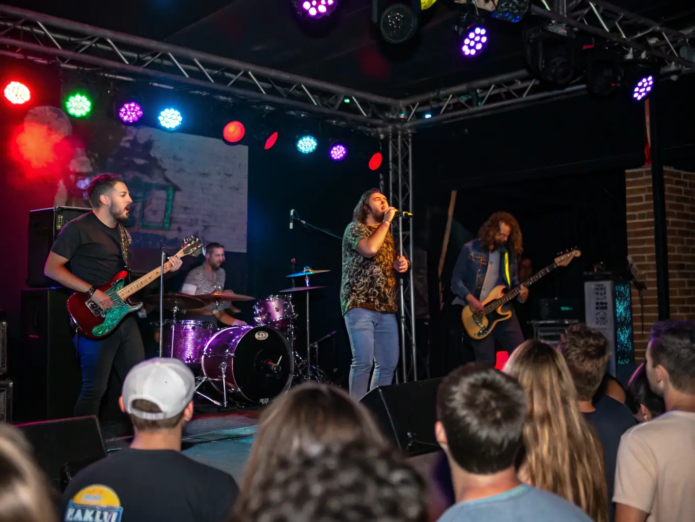 A vibrant photograph capturing the energy of a live performance supported by IMPASSYSTEM, featuring musicians on stage and an engaged audience in the foreground.